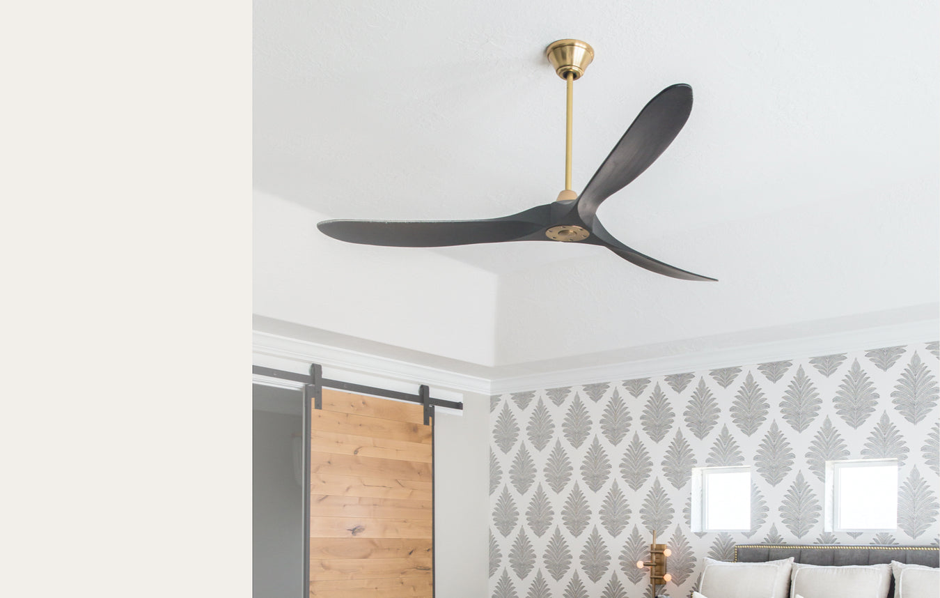 A sleek, modern black ceiling fan with brass in a white and gray room.