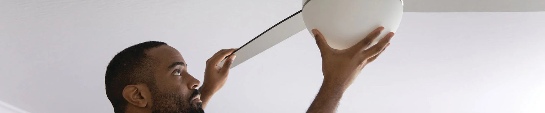 Shows a man reaching up to install a ceiling fan