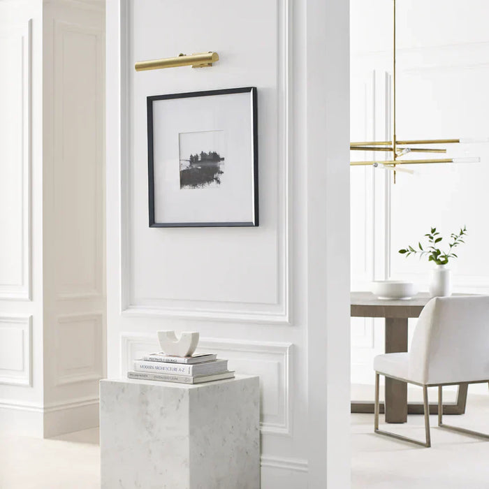 Shot of a white wall with a gold picture light hanging over a black and white picture frame