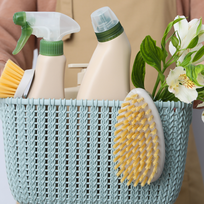 A person holds a light blue basket filled with cleaning supplies and flowers