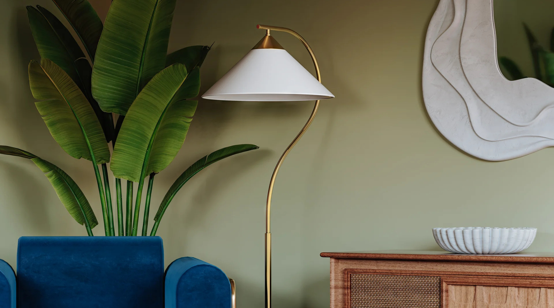 Floor lamp with white shade against a green wall and over a blue velvet armchair