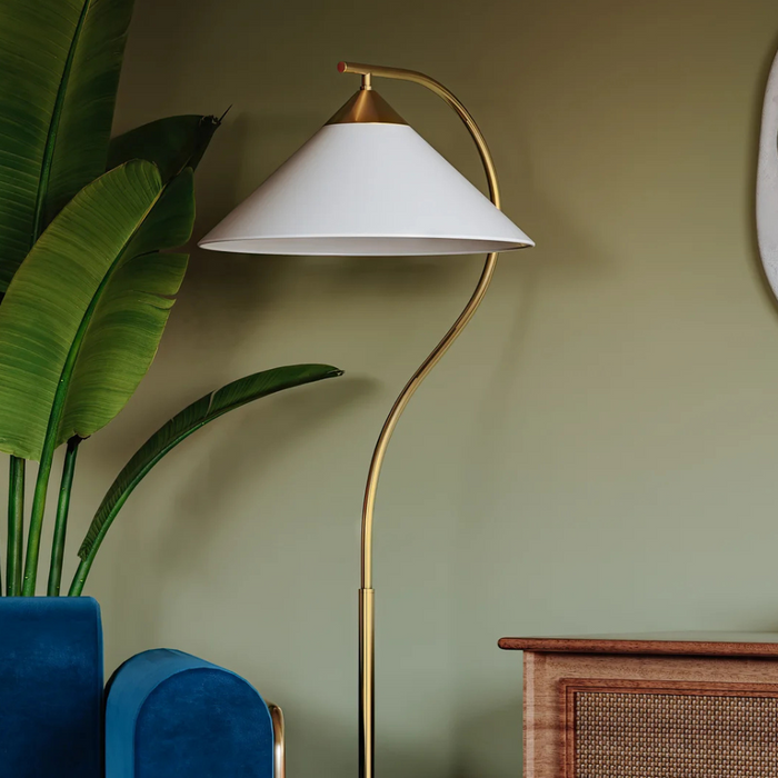 Floor lamp with white shade against a green wall and over a blue velvet armchair