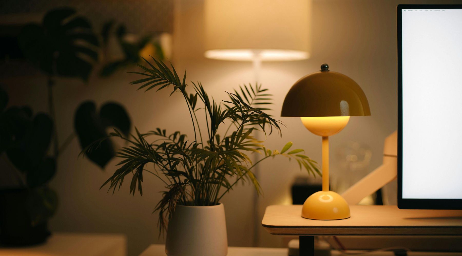 Table lamp with warm lighting sits on a desktop. Behind it a white floor lamp glows