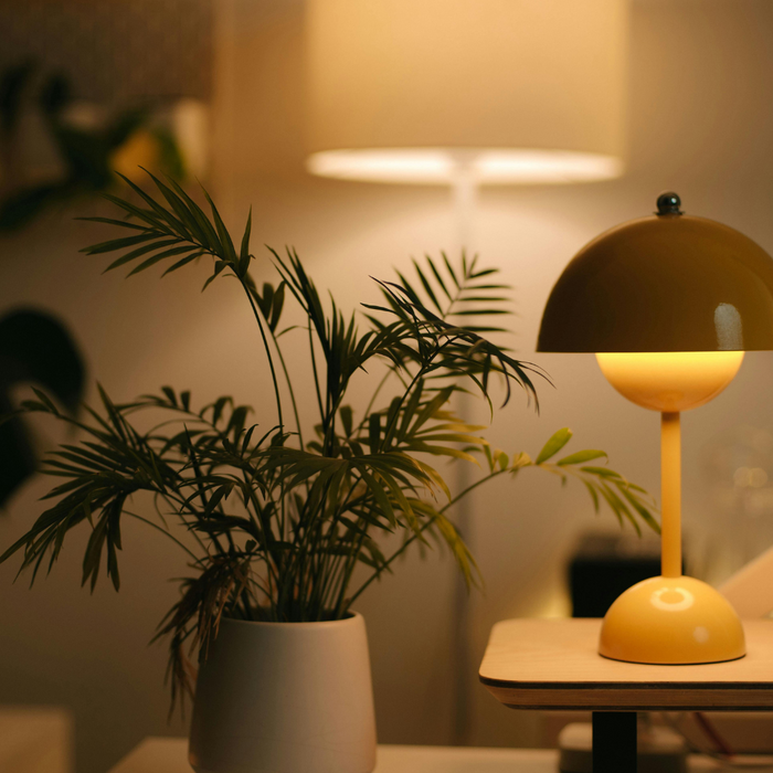 Table lamp with warm lighting sits on a desktop. Behind it a white floor lamp glows