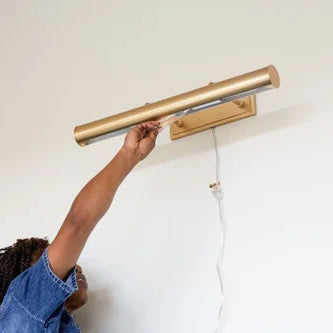 Woman screwing in a light bulb to a picture light on the wall