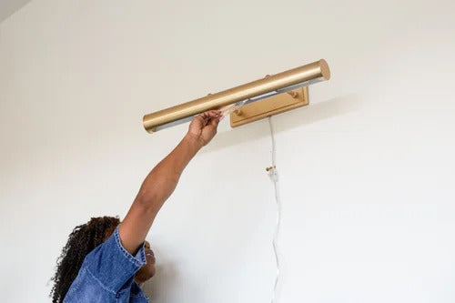 Woman screwing in a light bulb to a picture light on the wall