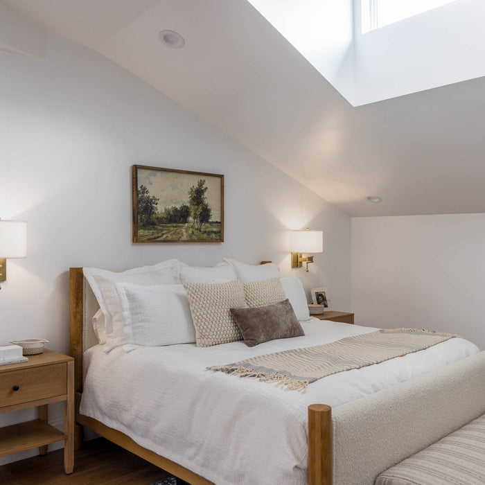 Attic-style bedroom with sloped ceilings, wall-mounted sconces, neutral bedding, and wood furniture.