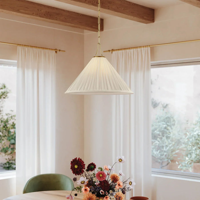 A pleated white shade pendant hangs over a dining room table in front of two large windows
