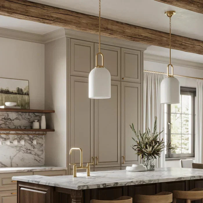 Warm modern kitchen with marble island, beige cabinets, brass fixtures, and two white pendant lights hanging above the counter.