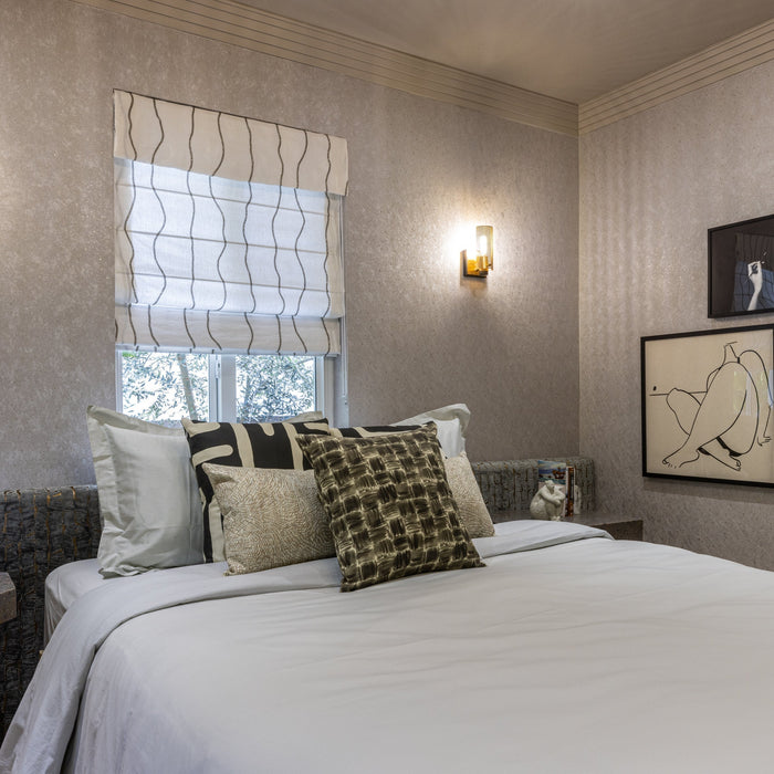 Bed against a grey wallpapered wall and two gold sconces on either side