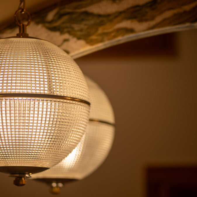 Two spherical pendant lights with textured glass shades and warm brass accents hang in front of a marble backsplash, casting a soft, warm glow that creates an elegant and inviting atmosphere.