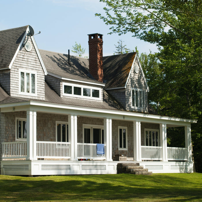 Large grey and white home with white wrap-around porch. A green lawn and large green tree sit nearby