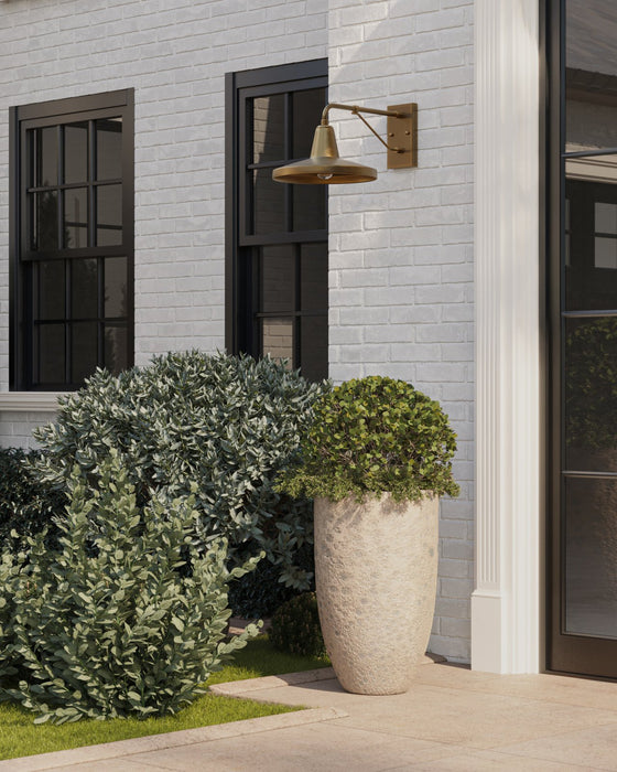 Decorative outdoor planters with greenery in front of a building with a wall-mounted light fixture.