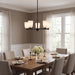 A modern multi-light chandelier with five warm white glass shades and a black frame hangs over a wooden dining table set for four in a bright, neutral-toned dining room.