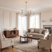 A styled living room featuring a beige fabric sofa, two matching armchairs, a round wooden coffee table, a wooden sideboard, and a multi-light chandelier hanging from a central ceiling.
