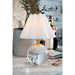 Table lamp with a glass base and white shade on a marble surface.