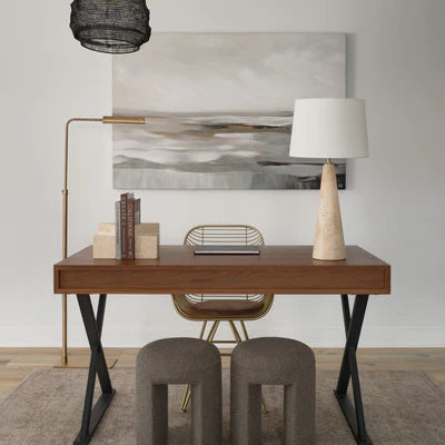 Modern workspace with a wooden desk, sculptural stools, abstract wall art, and a stone-base table lamp beside a brass floor lamp.