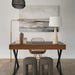 Modern workspace with a wooden desk, sculptural stools, abstract wall art, and a stone-base table lamp beside a brass floor lamp.