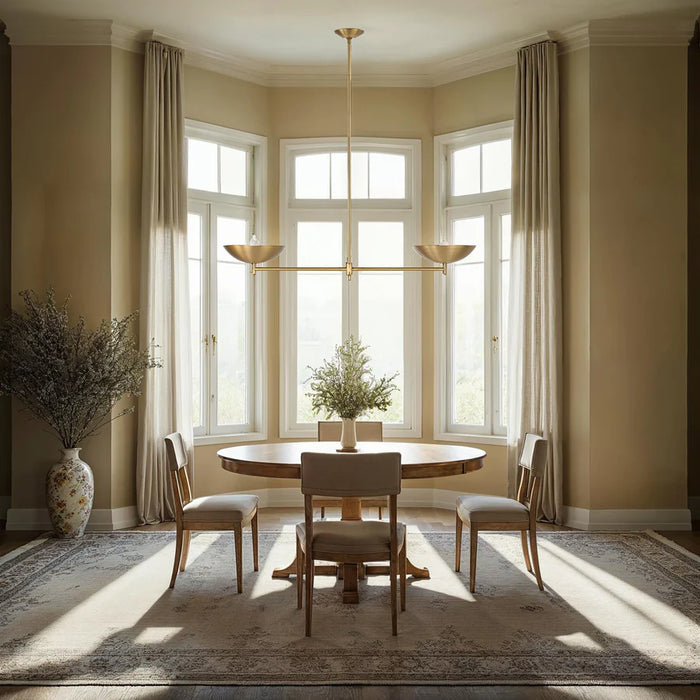 Elegant dining room with a modern brass linear chandelier, round wood table, and tall sunlit windows.