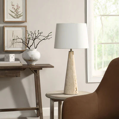 Modern stone-base table lamp with a white fabric shade placed on a round side table beside a brown accent chair.