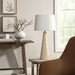 Modern stone-base table lamp with a white fabric shade placed on a round side table beside a brown accent chair.