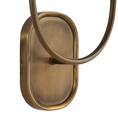 Close-up of an antique brass wall sconce backplate with curved metal arm detail.
