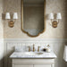 Classic bathroom vanity with marble countertop, gold-framed mirror, and matching brass double wall sconces with white shades.
