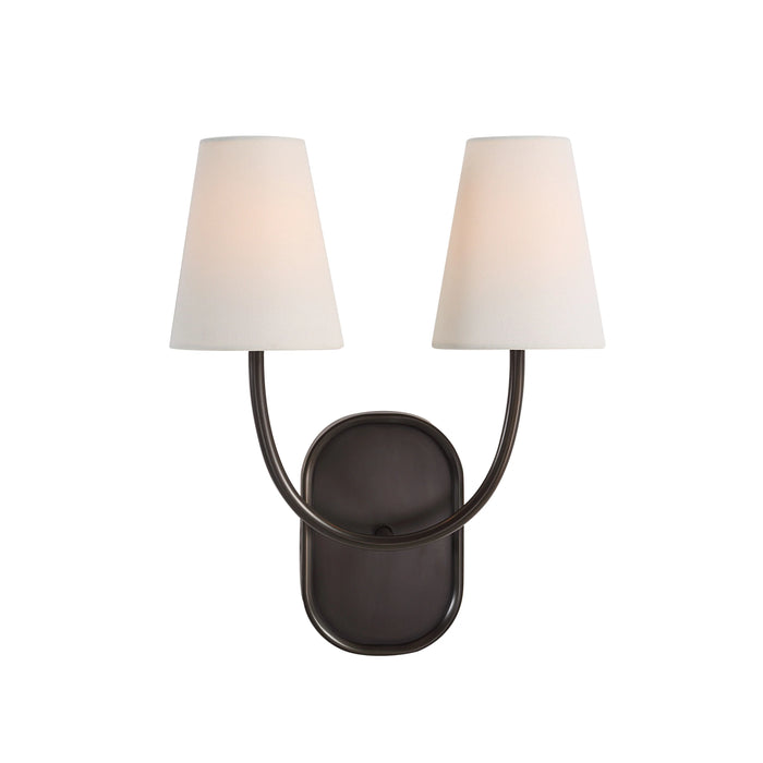 Dark bronze double wall sconce with curved arms and white tapered fabric shades illuminated.