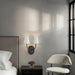 Modern bedroom corner with dark bronze double wall sconce, upholstered chair, and soft ambient lighting.