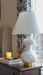 White lamp on a wooden surface with a candle and decorative tray in the background.