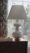 White lamp with a beige shade on a wooden dresser by a window