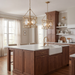 A modern kitchen interior with two gold geometric pendant lights hanging over a wood island with a white countertop and farmhouse sink.