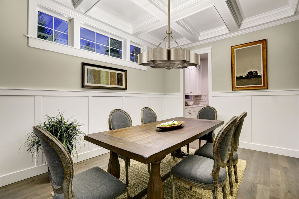 Dining room with wooden table and gray chairs, featuring a silver fandelier and framed pictures on the wall.