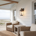 A black outdoor wall sconce with a warm glowing light, mounted on a white wood-paneled porch wall next to wicker furniture.