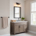 A rustic gray-brown wooden bathroom vanity with a white countertop, black faucet, and a black-framed mirror, set against a white subway tile wall in a bright bathroom.