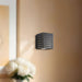 Black square wall light fixture on a beige wall with a blurred background