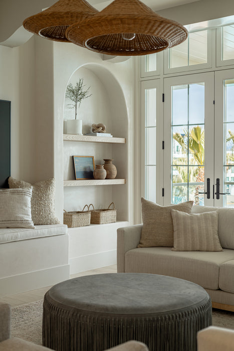 Bright living room with woven pendant lights, arched built-in shelves, neutral seating, and large French doors opening to an outdoor view.