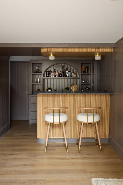 Modern bar area with wooden cabinets, stools, and a shelf with bottles.