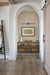 Arched hallway nook with a built-in wood console, decorative vases and artwork, wood flooring, and a minimalist picture light above the shelf.