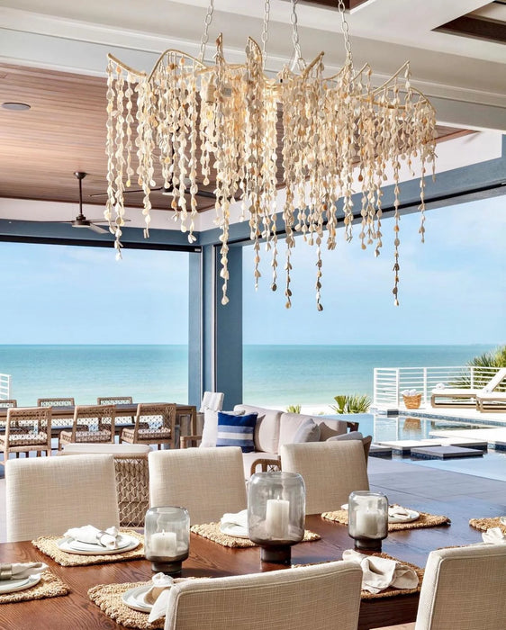 Elegant dining room with a large chandelier, table setting, and ocean view.