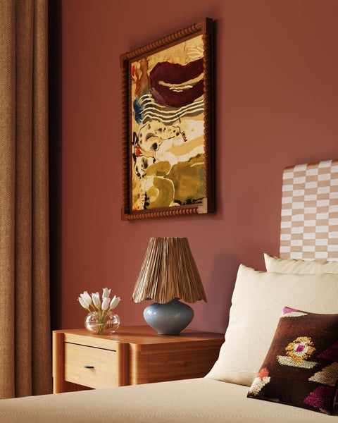 Decorative painting on a wall above a bedside table with a lamp and flowers in a bedroom.