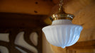 Vintage-style pendant light with white glass shade and gold fixture against a wooden wall.