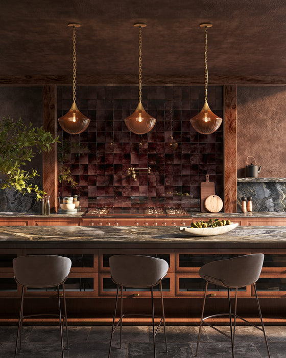 Three pendants hang over an island in a modern, moody kitchen
