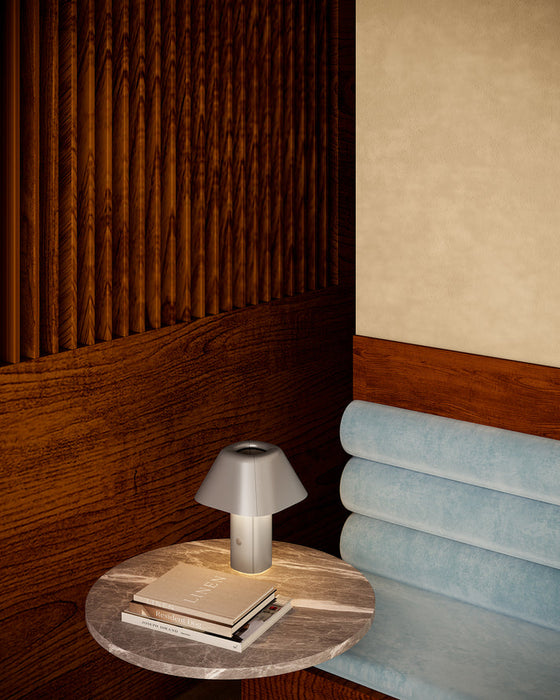 Round wooden table with a lamp and books next to a light blue sofa against a wooden wall.