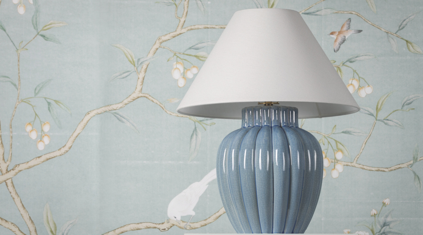 Blue ceramic table lamp with a white shade against a decorative wallpaper background