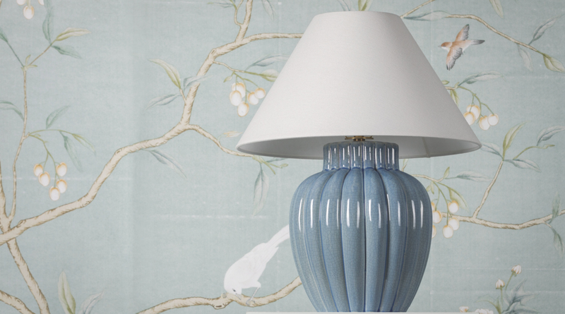 Blue ceramic table lamp with a white shade against a decorative wallpaper background