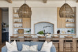 Open-concept kitchen with two large woven pendant lights hanging over a marble island, light wood cabinetry, open shelving, and a soft blue sofa in the foreground.