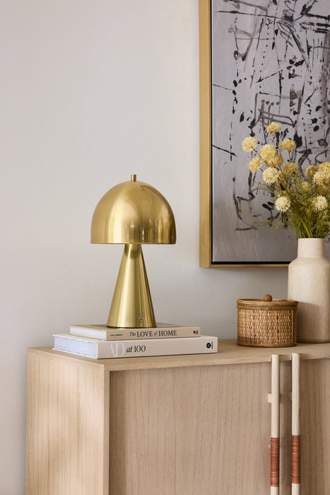 Gold lamp on a wooden console table with decorative items against a light wall.
