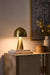 Gold table lamp on a wooden surface with books and a vase in the background