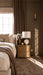 A nightstand sits next to a bed with neutral linens against a brown painted wall